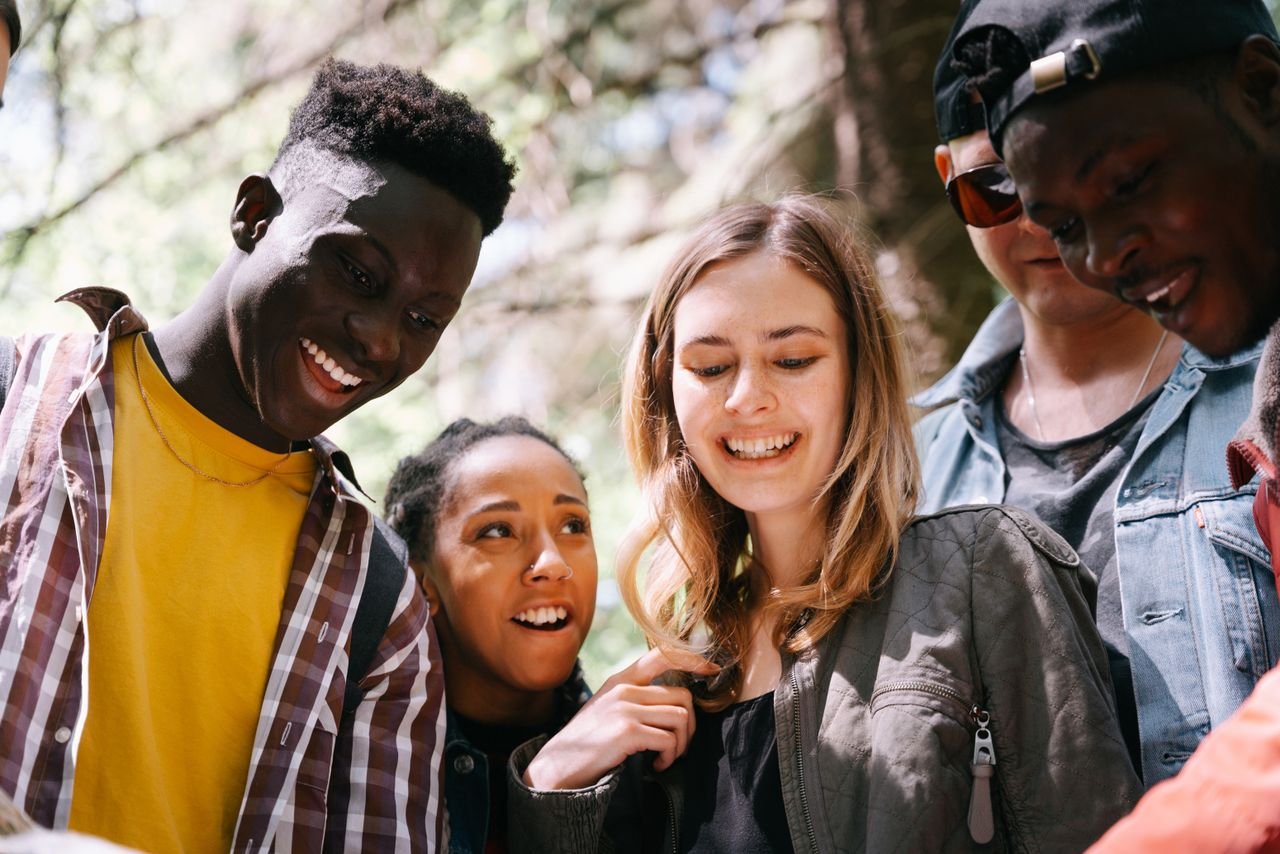 A group of diverse young adults enjoying a moment together outdoors, smiling and happy.